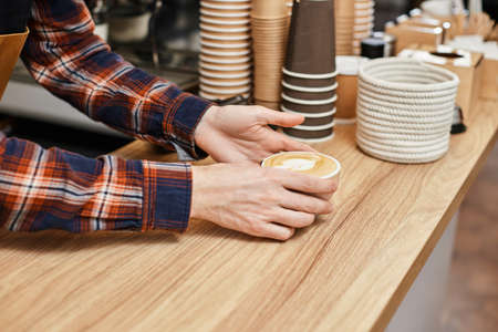 male waiter in apron holding cup of hot drinkの写真素材