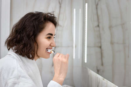 woman in white bathrobes brushing teeth in front of mirrorの写真素材