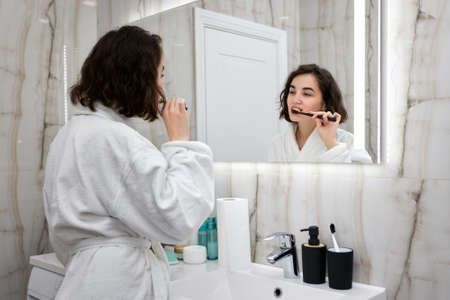 woman in white bathrobes brushing teeth in front of mirrorの写真素材