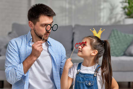 father and little child girl holding paper glasses on stick .の写真素材
