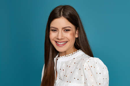 smiling young woman in white dress on blue background.