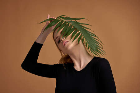 blonde woman holding exotic leaves near her faceの写真素材