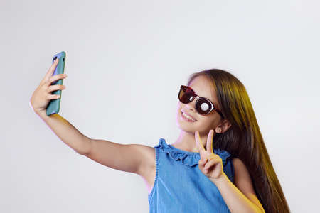 child girl showing victory sign while taking selfie on smartphoneの写真素材