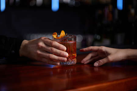 Barman holding out glass with alcoholic cocktail to the clientの写真素材