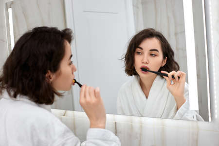 woman in white bathrobes brushing teeth in front of mirrorの写真素材