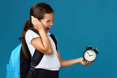 schoolgirl with backpack is holding alarm clock