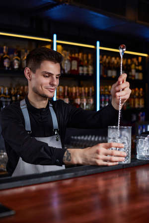 Barman stirring ice cubes in cocktail glass with spoon