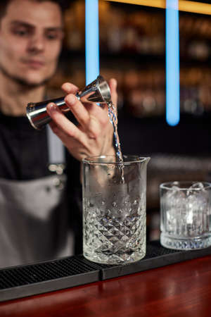 Bartender in apron adds ingredient to glassの写真素材