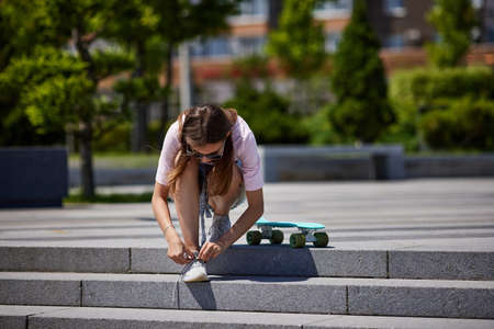 girl with skateboard sitting on steps and lacing up shoes