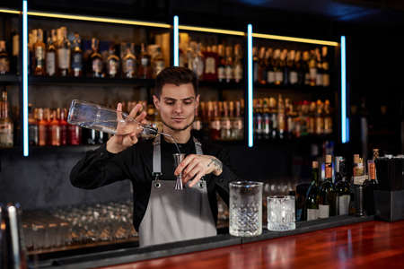 Bartender in apron adds ingredient to glassの写真素材