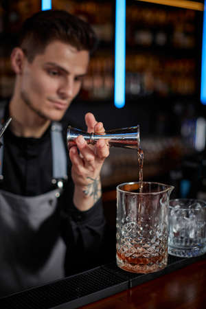 Bartender in apron adds ingredient to glassの写真素材