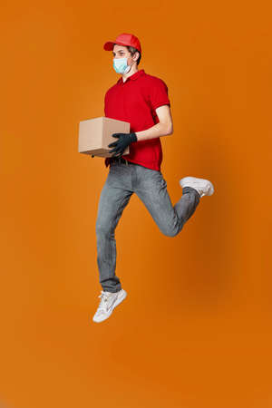 Delivery man in face mask holding cardboard box and jumpingの写真素材