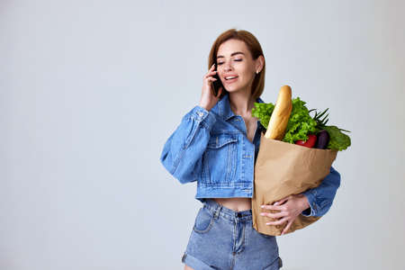 woman holding paper bag with vegetables and smartphoneの写真素材