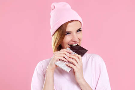 young happy woman in casual t-shirt biting sweet chocolate bar