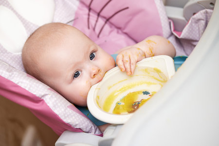 baby girl eating with spoon in kitchenの写真素材