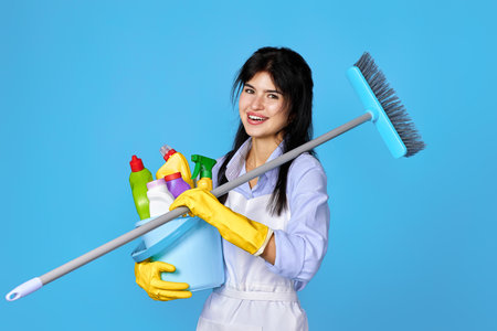 woman in gloves holding bucket of detergents and broomの写真素材