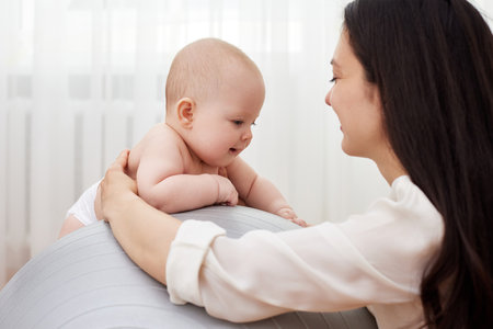 mother playing with her baby girl on a fitness ballの写真素材