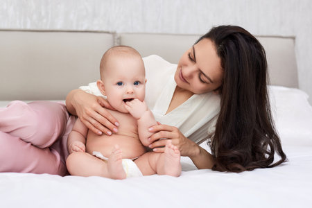 mother plays with her baby girl in the bedroom.
