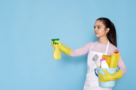 woman in rubber gloves and cleaner apron holding bucket of detergentsの写真素材