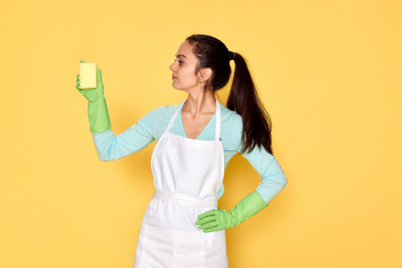 woman in gloves and cleaner apron cleaning with yellow spongeの写真素材