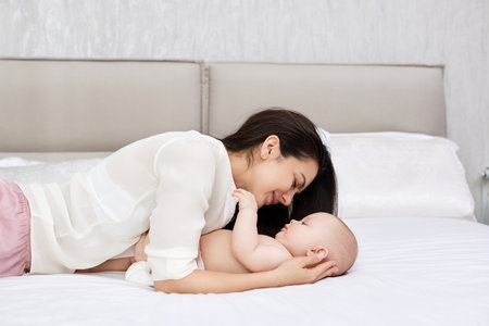 mother plays with her baby girl in the bedroom.
