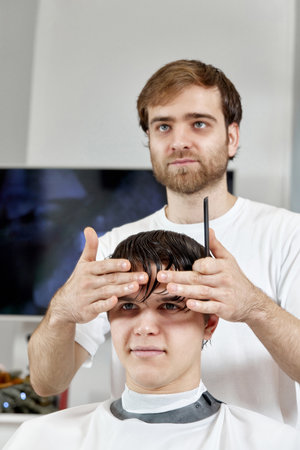 Barber talking to caucasian man while sitting in chairの写真素材