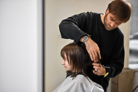 Professional male hairdresser cutting female hair in salon