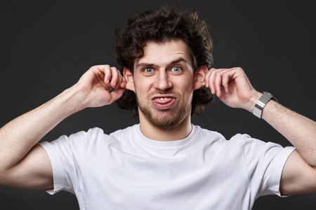 portrait of young funny curly man in white t-shirt grimacingの写真素材