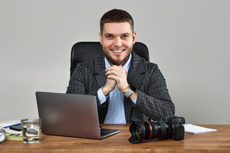bearded male photographer smiling while working at her desk.の写真素材