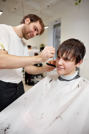 young caucasian man getting haircut by professional male hairstylistの写真素材