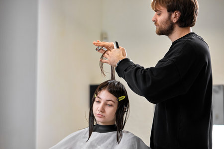 Professional male hairdresser cutting female hair in salonの写真素材