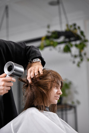 man hairdresser dries female hair with hairdryer after washingの写真素材