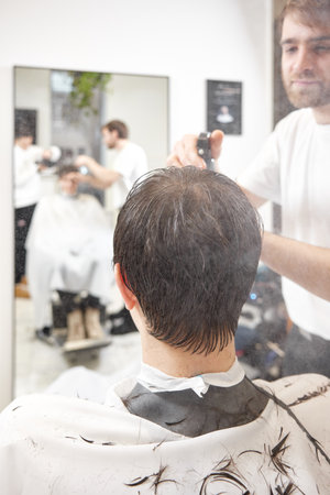 young caucasian man getting haircut by professional male hairstylistの写真素材