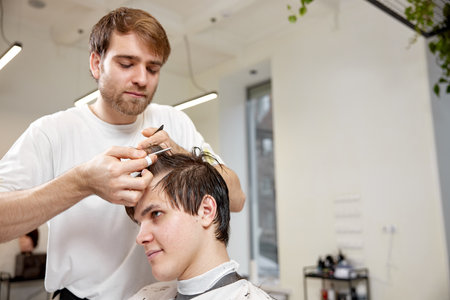 young caucasian man getting haircut by professional male hairstylistの写真素材