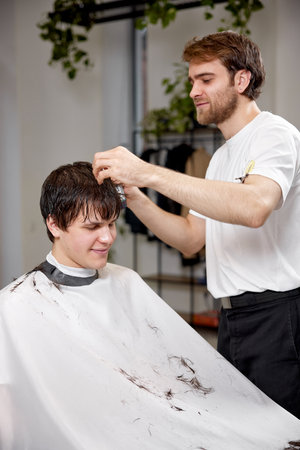 young caucasian man getting haircut by professional male hairstylistの写真素材
