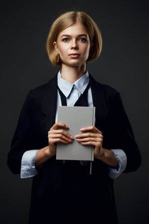 trendy blonde businesswoman holding notepad on black backgroundの写真素材