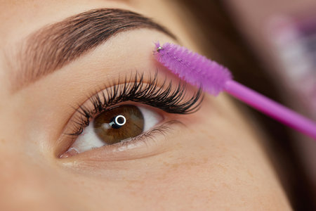 master combs the eyelashes of the client after the eyelash extension procedure. close-up....