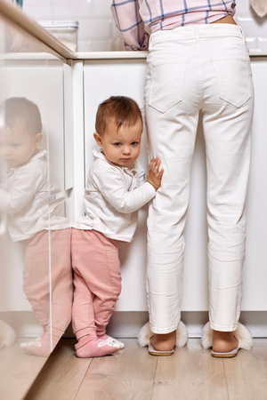 mother doing housework with her baby girl. woman cleaning dishes and kid is upset because she wants to playの写真素材