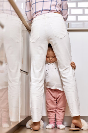 mother doing housework with her baby girl. woman cleaning dishes and kid is upset because she wants to playの写真素材
