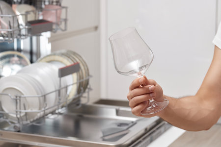 male hand takes wine glasses out of dishwasher in kitchen.の写真素材