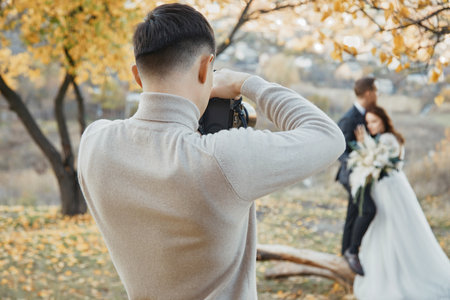 Professional wedding photographer taking pictures of the bride and groom in nature in autumnの写真素材