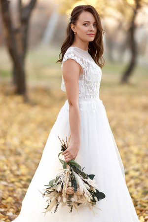 beautiful happy bride holding wedding autumn bouquet in natureの写真素材