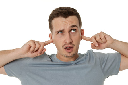 Young annoyed caucasian man in t-shirt covers ears with hands fingers on white backgroundの写真素材
