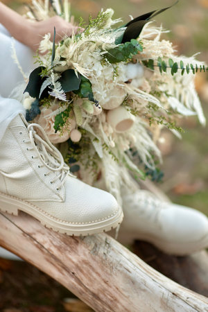 bride wearing white boots holding beautiful autumn bouquet.の写真素材