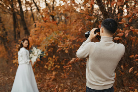 Professional wedding photographer taking pictures of the bride and groom in nature in autumnの写真素材