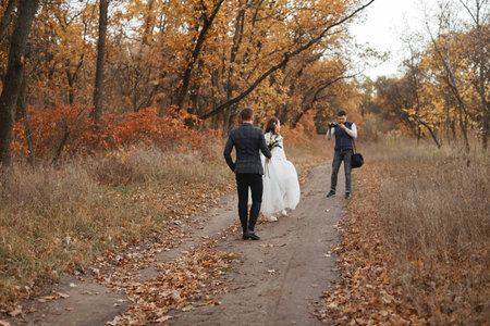 Professional wedding photographer taking pictures of the bride and groom in nature in autumnの写真素材