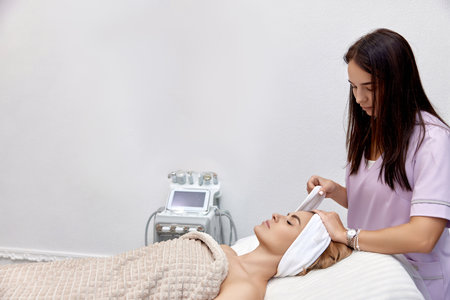 Cosmetologist putting white headband towel on female patient head in beauty salonの写真素材
