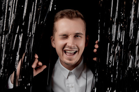 handsome man in black suit winking looking at the camera with happy expression on glitter background.の写真素材
