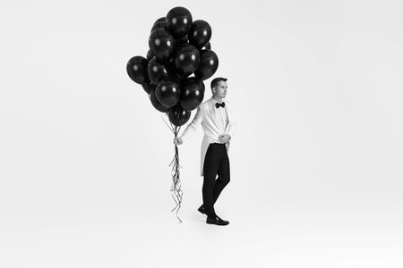 elegant caucasian man in white suit tuxedo with black air balloons on white background. Full sizeの写真素材