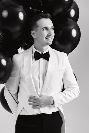 elegant caucasian man in white suit tuxedo with black air balloons on white background.の写真素材